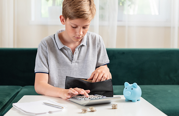 Kid teen boy counting money and taking notes, saving money in a piggy bank.