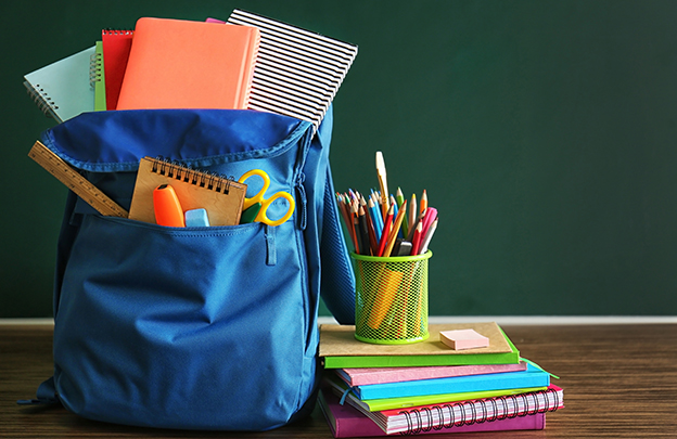 School backpack with accessories on chalkboard background